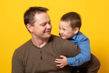 Happy father's day! Cute father and son hugging on yellow background. Portrait of a dad with a baby boy smiling and hugging. Family concept.の写真素材