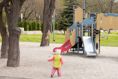 LIttle girl is played in the playground. Child in warm clothes walks in the playground
