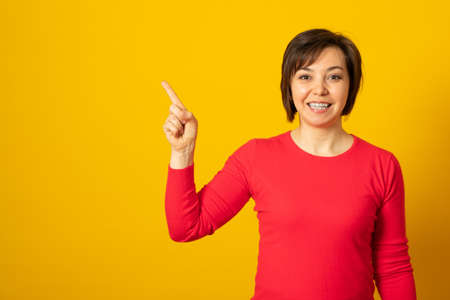 Positively surprised woman points upwards with broad smile, recommends awesome product, suggests click banner, dressed casually, shows advertisement promo.の写真素材