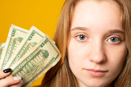 Portrait of a happy teen girl holding bunch of money banknotes and looking at camera isolated over yellow backgroundの写真素材