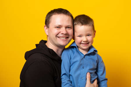 Happy father's day! Cute father and son hugging on yellow background. Portrait of a dad with a baby boy smiling and hugging. Family concept.の写真素材