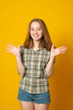 Optimistic girl raises palms from joy, happy to receive awesome present from someone, dressed in casual shirt, isolated on yellow background. Excited female happy.の写真素材