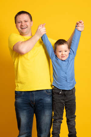 Young father and son hugging on yellow background. Portrait of a dad with a baby boy smiling and hugging. Family concept.の写真素材