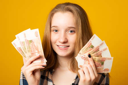 Happy beautiful young girl holding rubles money on yellow background. Sale, finance, banking, winning, economic, credit, business, shopping concept. RUB, Russian Ruble.の写真素材