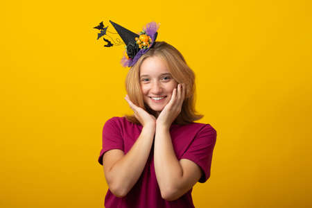 Halloween party girl. Happy Halloween witch with a black hat.  Cute young smiling woman in witches hat and costume on yellow background.の写真素材