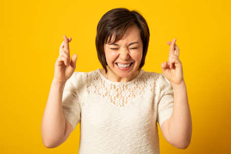 Worried beautiful young woman close eyes, crosses fingers as shows her desire for something to...