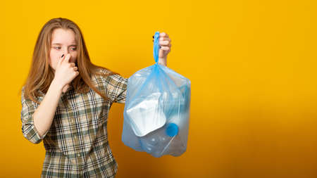 Banner copy space. Woman holding a smelly garbage bag on yellow background.の写真素材