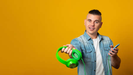 Banner copy space. Portrait of a handsome man with earphones holding mobile phone isolated on the yellow background.の写真素材