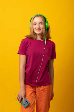 Happy girl listens music in headphones holds mobile phone chooses song from playlist dressed in casual t-shirt.の写真素材