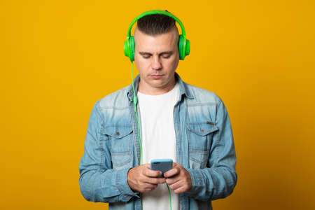Happy man with earphones holding smartphone isolated on yellow background.の写真素材