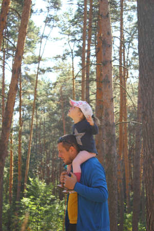 father carries an enthusiastic daughter on his shoulders in a sunny forestの写真素材