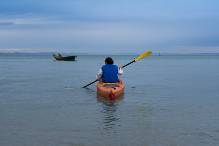 The girl goes towards the boat in her kayaks.