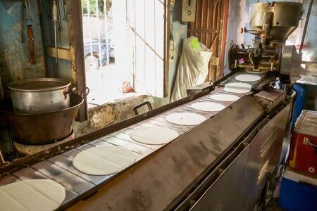 Corn tortillas are coming out of the machine very hot and tasty.の写真素材