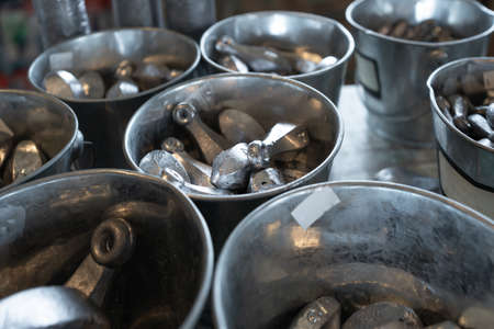 On the table there are many buckets with a lot of lead fishing sinkers.
