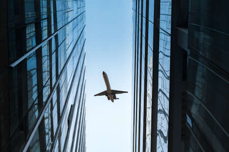 upward view of modern glass skyscraper and airplaneの写真素材