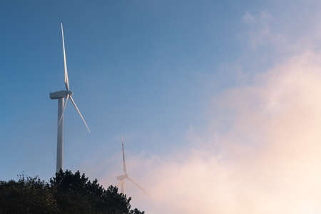 wind turbines closeup in early morning ,clouds and mist involve the mountain topの写真素材