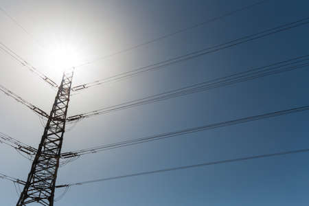electric power pylon silhouette under the sun over blue skyの写真素材