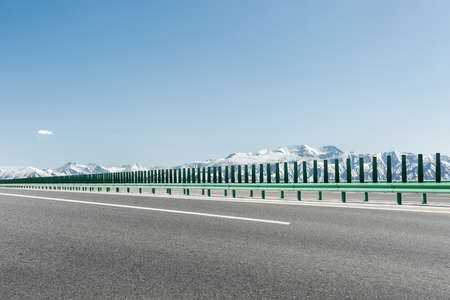 highway with snow mountain background against a sunny skyの写真素材