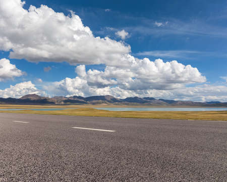 empty asphalt road and plateau lake against a blue sky, qinghai province, Chinaの写真素材