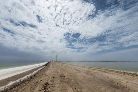 salt lake and dirt road against cloudy sky, qinghai province, Chinaの写真素材