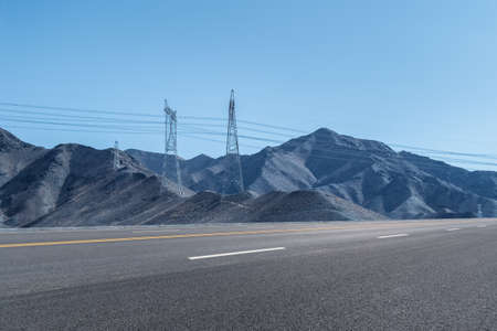 empty highway with power transmission tower on the mountain against a blue sky, road backgroundの写真素材