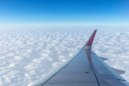 plane wing above the thick clouds, sky scene outside the porthole of an airplaneの写真素材
