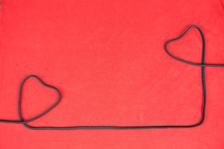 Heart shaped black rope on red background.の写真素材