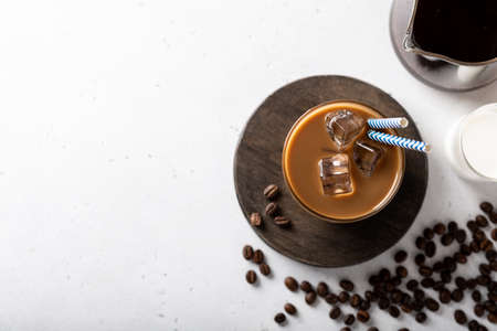 ice coffee with ice cubes in a glass on a light background, coffee beans are scattered nearbyの写真素材