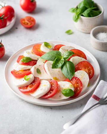 Italian caprese salad with sliced tomatoes, mozzarella, basil, olive oil on a light background.の写真素材