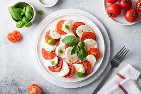 Italian caprese salad with sliced tomatoes, mozzarella, basil, olive oil on a light background. Top view.の写真素材