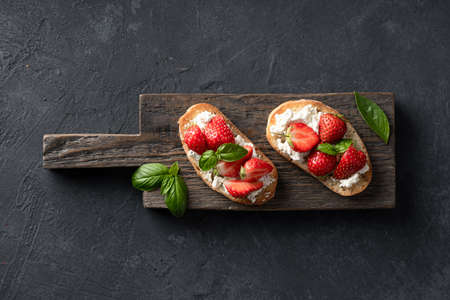 Bruschettas with strawberries, cream cheese and basil on a wooden board on  blackの写真素材