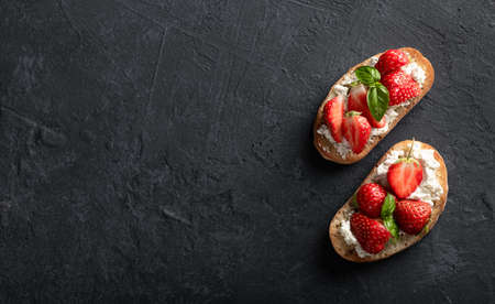 Bruschettas with strawberries, cream cheese and basil on a blackの写真素材