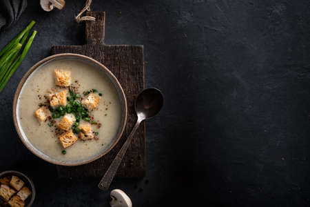 mushroom cream soup with champignons and croutons in a ceramic bowl on a black background, top view, place for textの写真素材