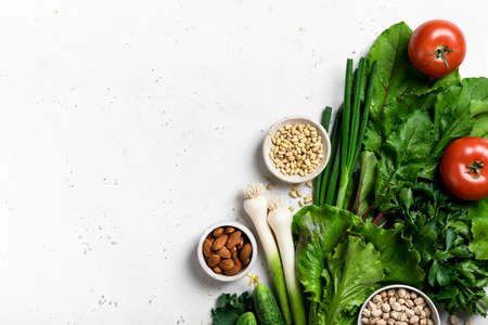 Healthy vegan food concept. Fresh vegetables, herbs and nuts on a light background, border, top view
