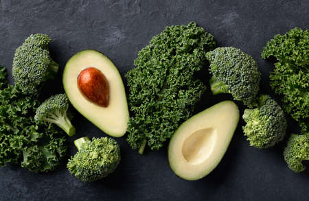 Avocado, kale and broccoli, detox dieting concept. Green vegetables on a dark stone background, top...