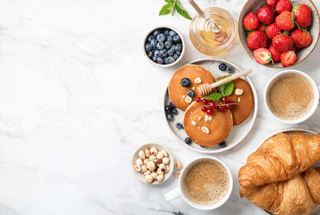 breakfast top view, pancakes, croissants, berries, nuts and coffee on a white marble background