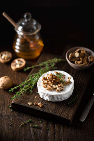 brie or camembert cheese with walnuts and honey on a wooden cutting board . Selective focus, dark backgroundの写真素材
