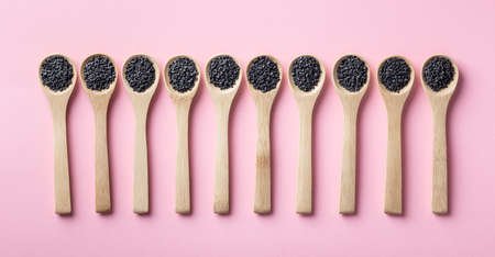black sesame seeds in wooden spoons on a pink background, top viewの写真素材