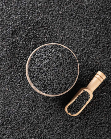 Black sesame seeds in a ceramic bowl and wooden spoon