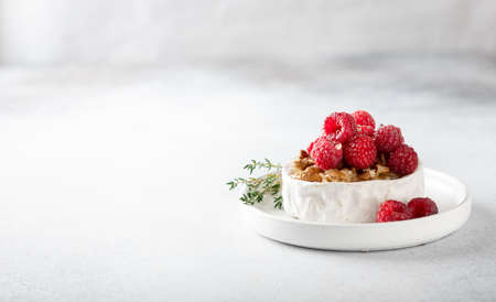 brie or camembert cheese with raspberries, honey, walnutsw and thyme . Selective focus, white background, copy spaceの写真素材