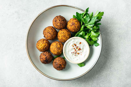 falafel balls with sauce in a ceramic bowl on a concrete background, top view