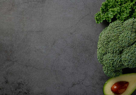 Avocado, kale and broccoli, detox dieting concept. Green vegetables on a dark stone background, top...