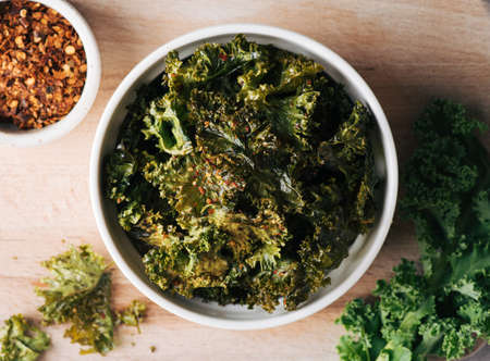 Kale chips in a ceramic bowl on wooden background, selective focus, top viewの写真素材