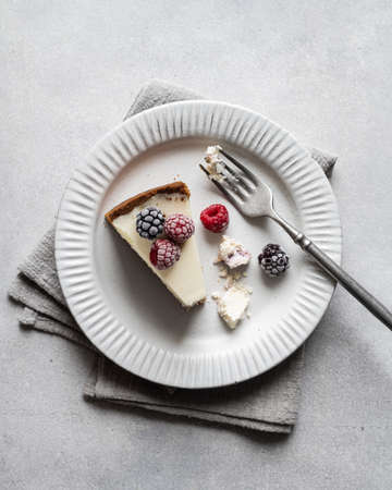 broken piece of cheesecake with frozen blackberries and raspberries on a white ceramic plate , top viewの写真素材