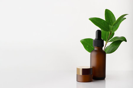 Dark glass bottle and cream, cosmetic products. In the background is a branch with leaves. Selective focus, copy spaceの写真素材