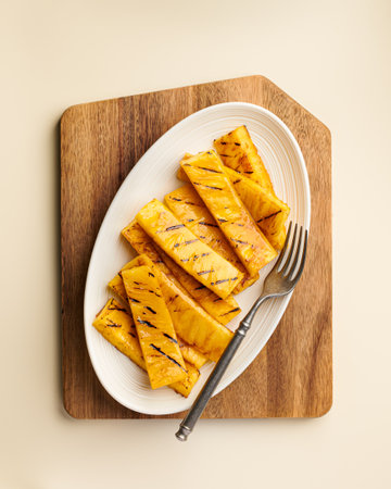 Beautifully grilled pineapple slices are artistically arranged on a pristine white plate, creating a tropical charmの写真素材