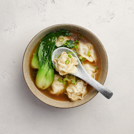Wonton soup with bok choy in dark bowl on light background, top viewの写真素材