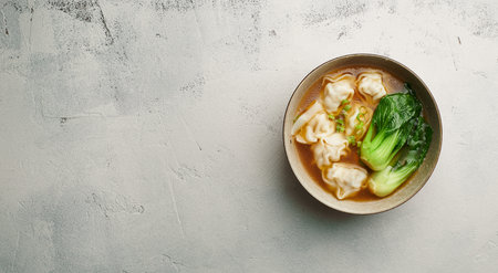 Wonton soup with bok choy in dark bowl on light background, top view, copy spaceの写真素材