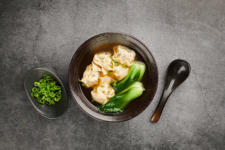 Wonton soup with bok choy in dark bowl on light background, top viewの写真素材