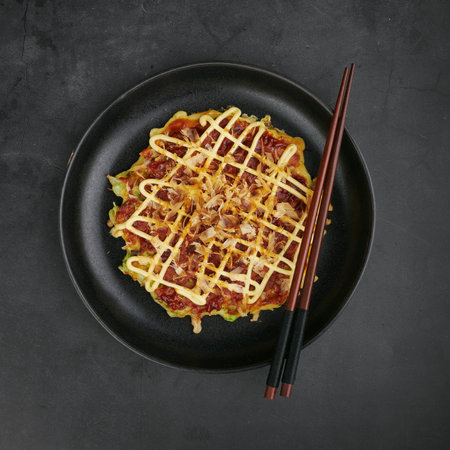 Japanese okonomiyaki pancake with mayo and bonito flakes on black plate, top view